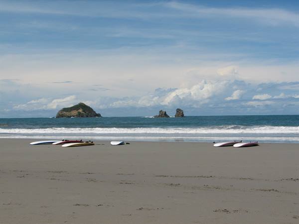Surfboards on the sand, waves and rocks in the Pacific, cloudy sky