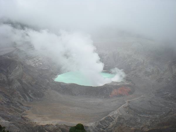 Turquoise lake inside Poás volcano crater, shrouded in smoke and mist