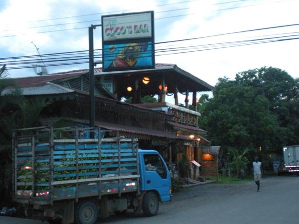 Blue truck loaded with bananas parked outside wooden Coco's Bar with lights on