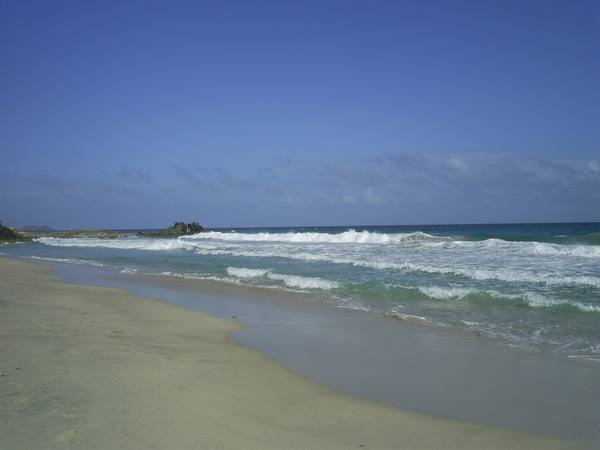 White waves breaking on pale sand under a blue sky