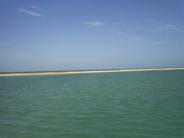 Emerald green water in front of a white sand strip under blue sky