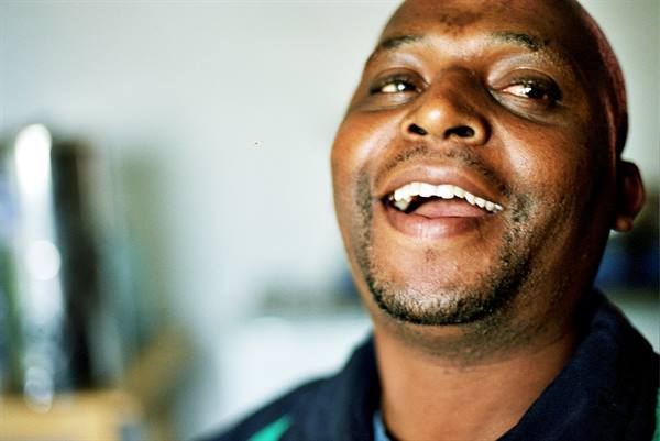 Close-up portrait of a smiling man indoors, natural light from the window