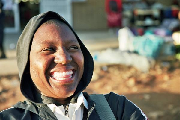 Young woman in black hoodie smiles at outdoor market, sunlight