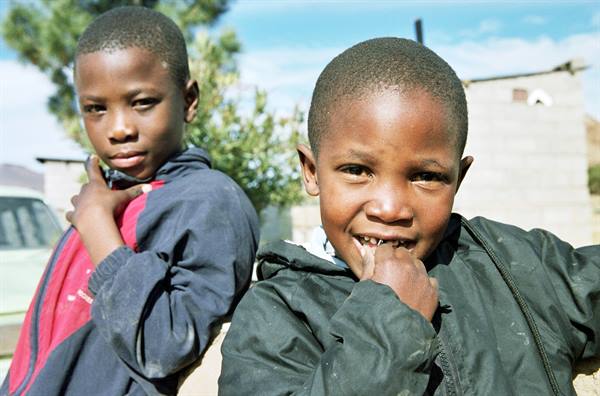Two smiling boys in jackets in front of concrete houses and trees