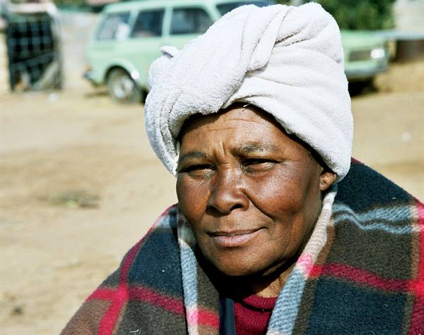 Woman in white towel turban and plaid blanket, green car behind