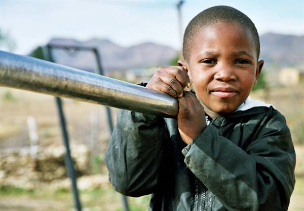 Smiling boy gripping a metal pipe, mountains and houses in the background