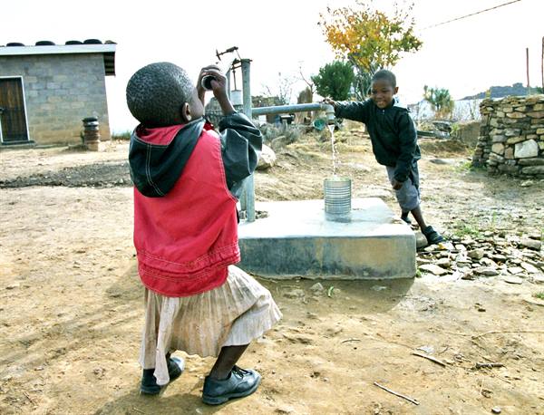 Children fill a bucket with water from a hand pump