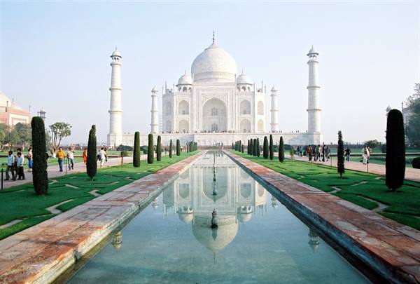 White marble Taj Mahal reflected in the long pool, visitors strolling the gardens