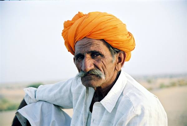 Elderly man wearing orange turban and white mustache, light shirt, natural daylight