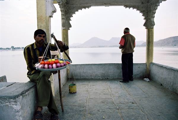 Vendor holding tray of toys under marble pavilion by the lake, Udaipur