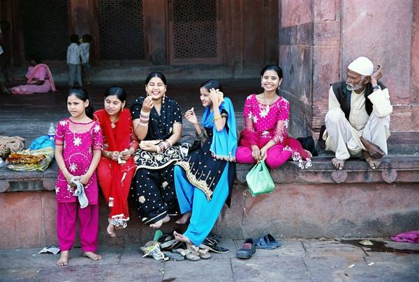 Women in colorful saris laughing on red sandstone steps beside a man