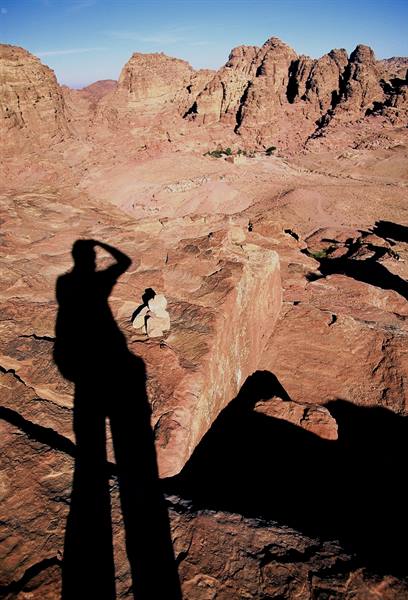Photographer's shadow cast on red rocks, trail above Petra