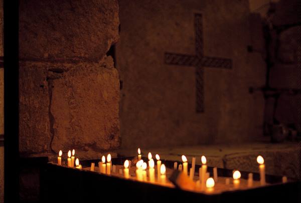 Candles burning before a cross carved in stone inside a church