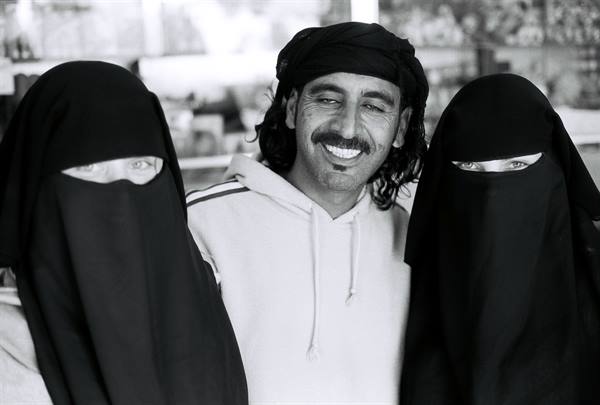 Smiling man in headscarf flanked by two women in black niqab