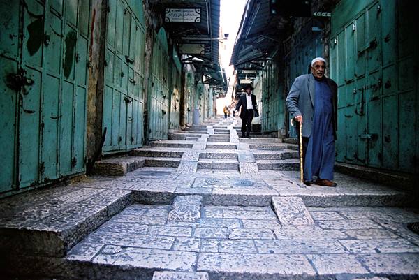 Elderly man with cane on stone steps between closed shops, Jerusalem