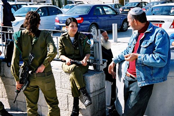 Two Israeli soldiers with rifles chat on the street with a bearded man
