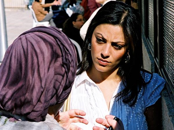 Dark-haired woman beside a woman in purple headscarf, in sunlight