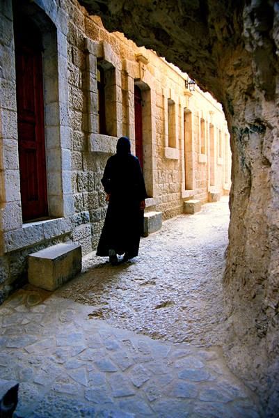 Woman in black robe walks past old limestone houses in an alley