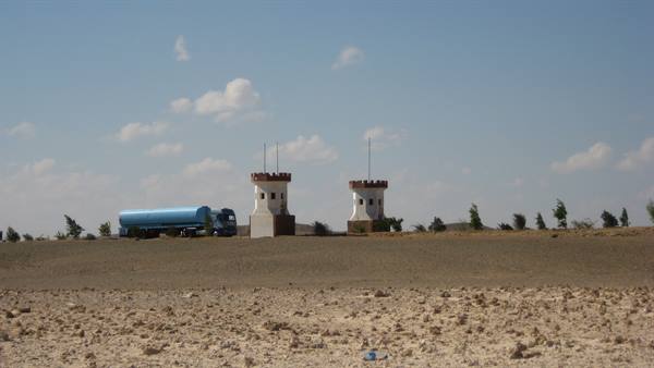 Blue tanker truck beside two white crenellated towers in rocky desert