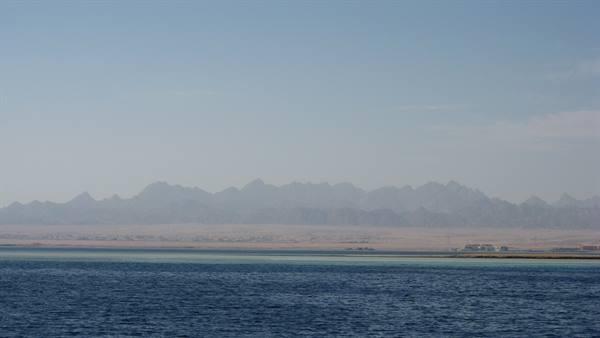 Hazy brown mountains rising above sandy shore and turquoise Red Sea waters