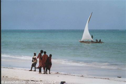 Fishermen on white-sailed dhow near beachgoers on Zanzibar beach