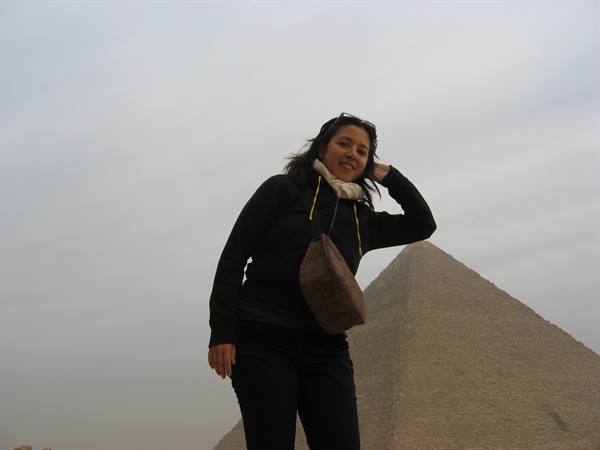 Smiling woman posing in front of the Great Pyramid of Giza under gray sky