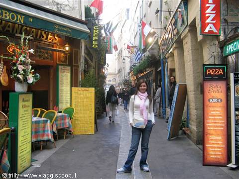 Smiling girl in a narrow Paris alley among creperies and pizza signs