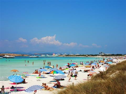 Tourists with colorful umbrellas on white sand, turquoise water, boats on horizon