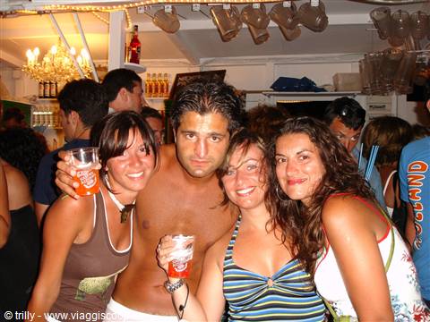Four smiling friends with drinks at a crowded night bar