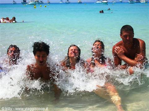 Group of young friends splashing in turquoise sea with anchored boats