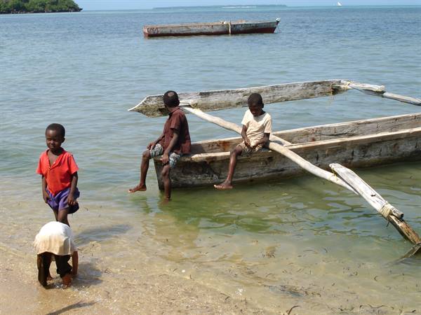 Children playing beside wooden outrigger canoes on the shore