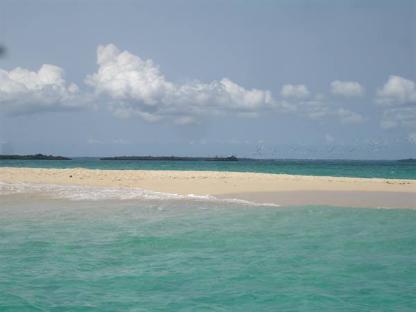 White sandbar surrounded by turquoise water, islands and clouds on the horizon