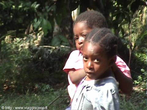 Two African children among green vegetation, one looking at the camera