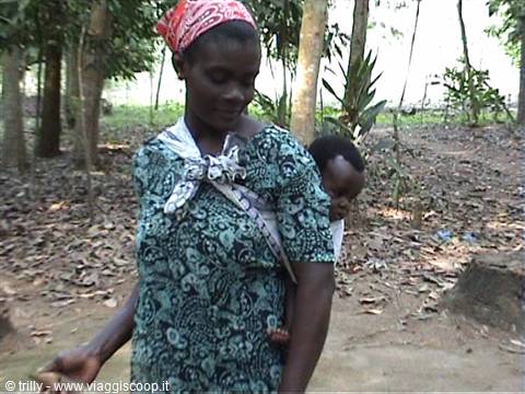 Woman in red bandana carries a baby on her back with cloth