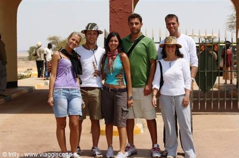 Group of tourists posing under an archway, metal gates and sand behind