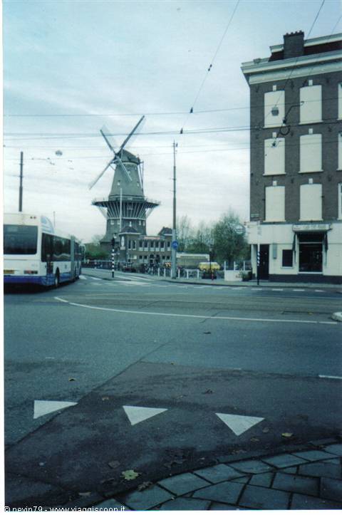 Brick windmill among tram wires, a bus and canal houses in Amsterdam