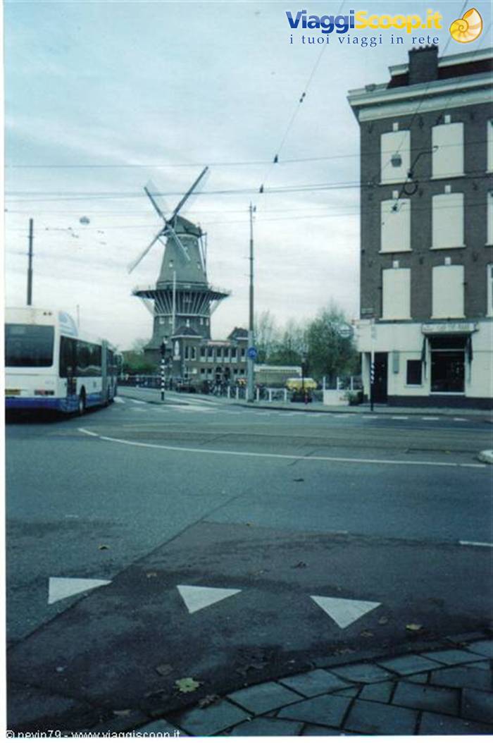 Brick windmill among tram wires, a bus and canal houses in Amsterdam