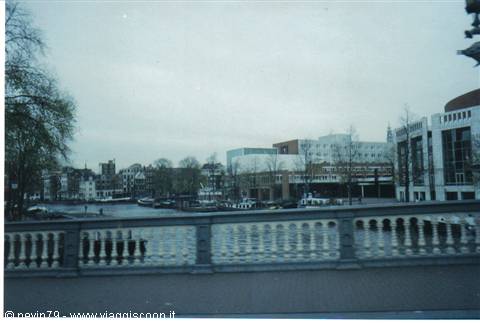 Amsterdam canal seen from stone bridge, houses and Stopera building under grey sky