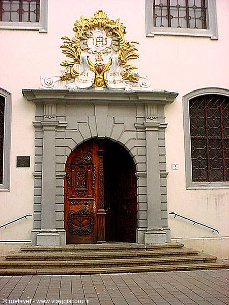 Grey stone portal with golden coat of arms and carved wooden door