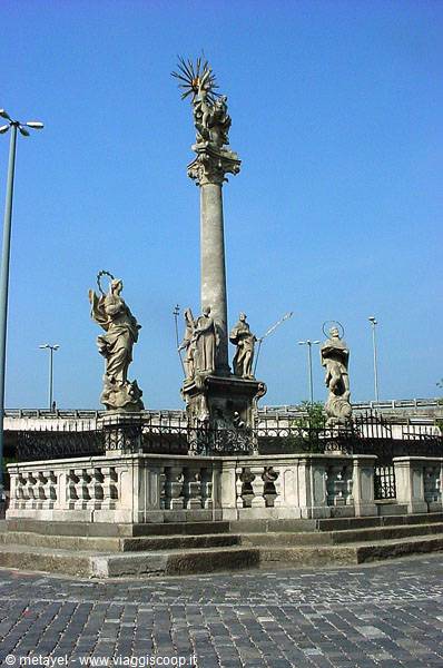 Baroque stone column with golden saints on fenced base, blue sky
