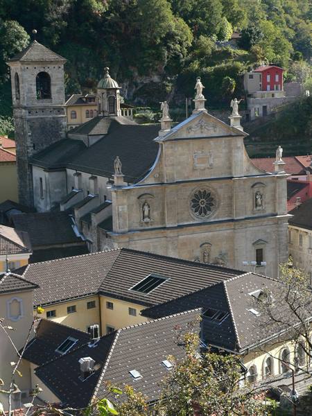 Stone church with rose window and statues, grey rooftops, bell tower, Bellinzona