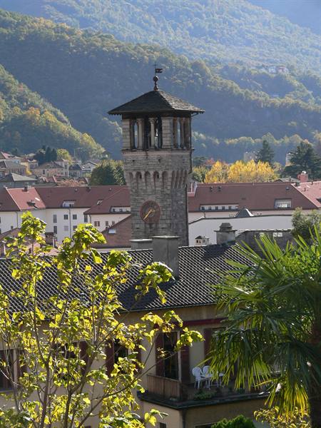 Stone clock tower with wooden roof rising above red tiled rooftops