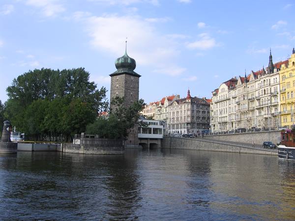 Green-domed tower on the Vltava River in Prague, historic buildings along the embankment
