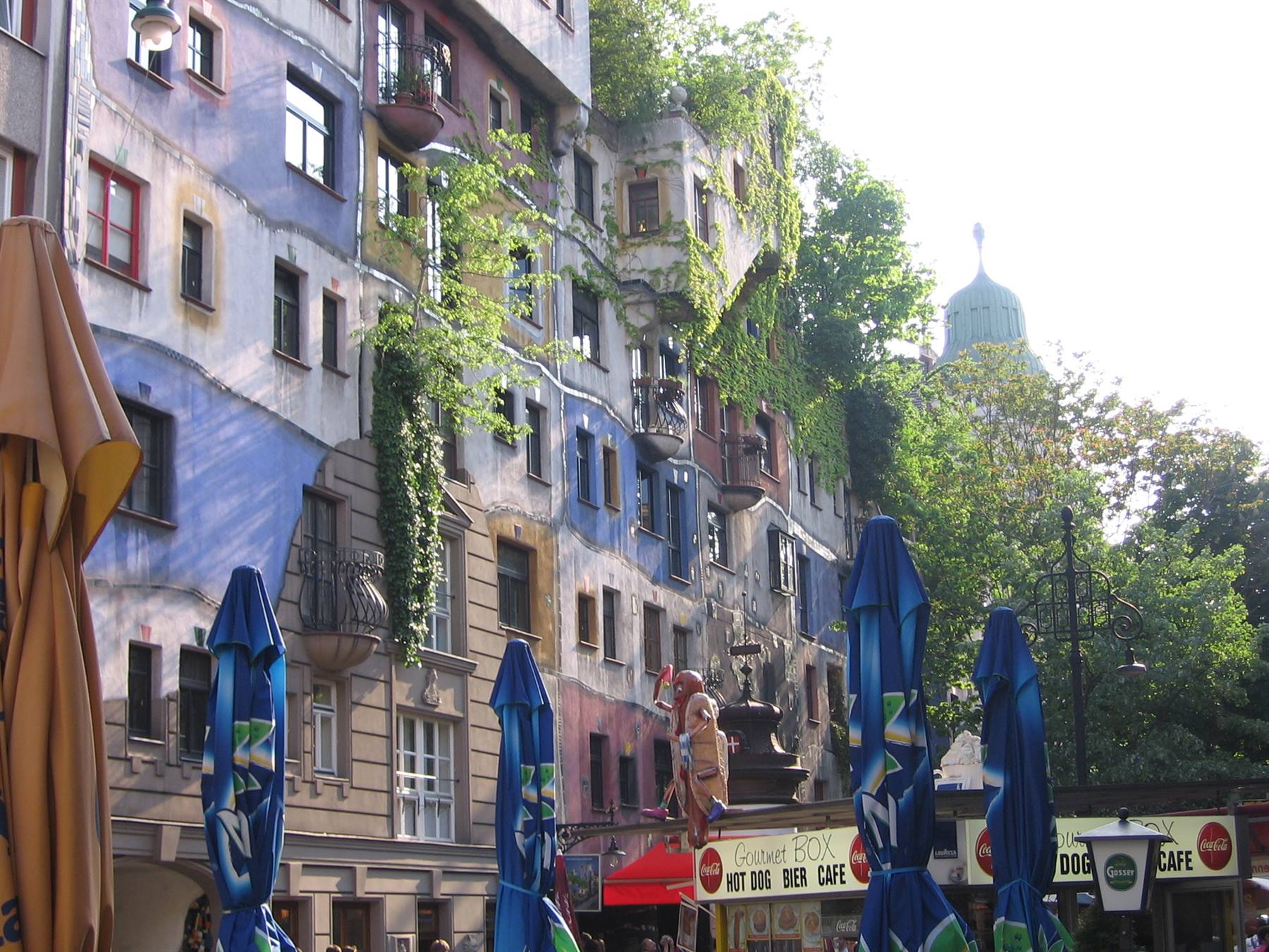Colorful plant-covered facade of the Hundertwasserhaus, closed umbrellas in front of food stalls