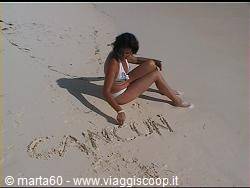 Girl sitting on white sand writing Cancún with her finger