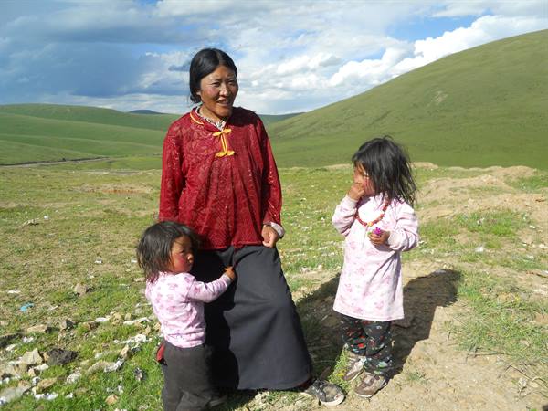 Tibetan woman in red with two little girls on grassy hills