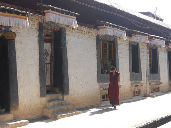 A monk in maroon robes walks past a Tibetan monastery with black-framed windows