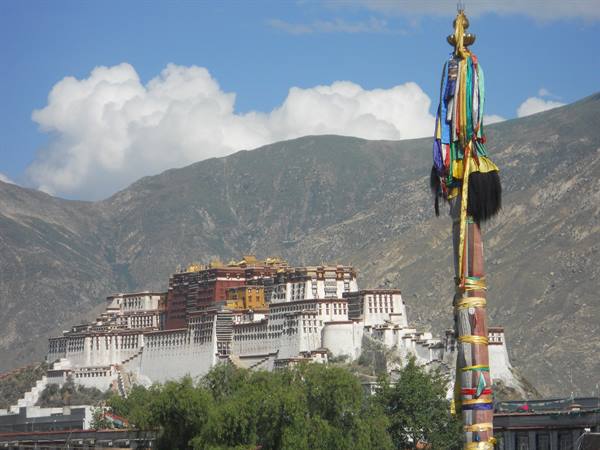 The Potala Palace in Lhasa among mountains and trees, with a prayer pole of colorful ribbons