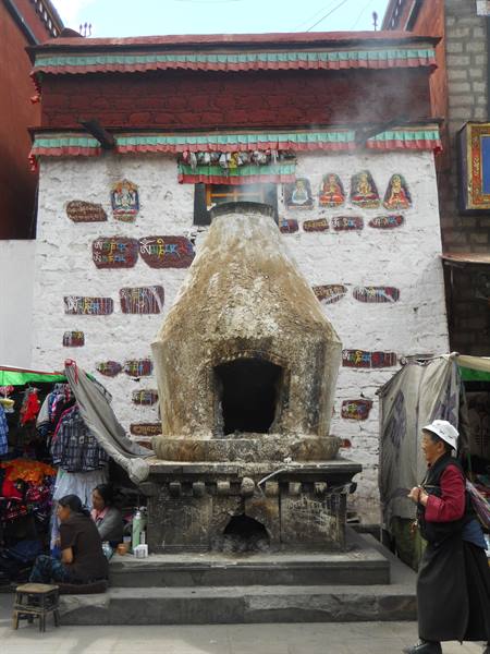 Smoking stone incense furnace before white mantra wall, pilgrims nearby