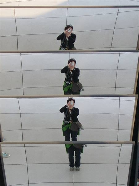 Woman with bag photographed four times in reflective mirrors above light tiles